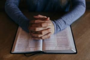 Crossed hands over a bible for prayer at Adult & Teen Challenge